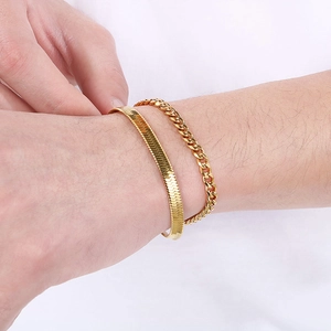 Detail of double-layered gold titanium steel flat snake and cuban link bracelets on wrist