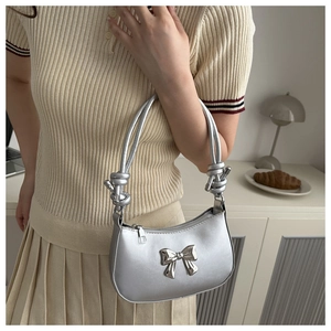 Detail of silver metallic underarm bag with a 3D bow and unique knotted shoulder strap