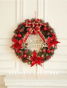 Close-up of lighted Christmas wreath with red flowers, gold bows, and pine cones
