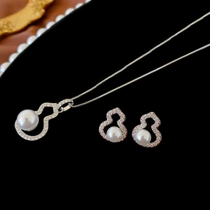 Macro shot of silver pearl hollow gourd necklace and earrings set on black velvet