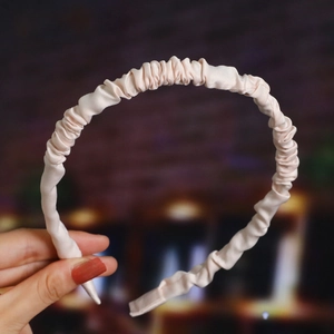 Detail of a pink satin headband featuring a pleated texture design held in hand