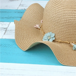 Détail d'un chapeau de paille orné de fleurs pastel et d'un gland coloré élégant