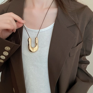 Dettaglio del ciondolo a U dorato su cordoncino marrone indossato con blazer elegante