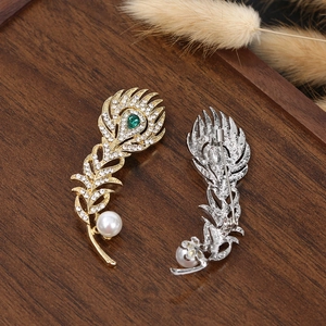 Vintage peacock feather brooch with green gemstone, white crystals, and pearl accent