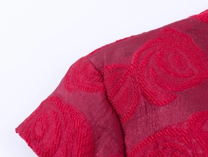 Détail du tissu en soie rouge avec broderie de rose sur l'épaule et la couture