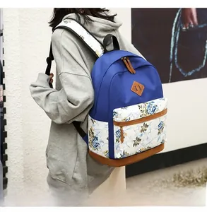 Detail of blue canvas backpack with floral patterns and leather patches on a model