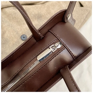 Detail view of the silver zipper closure and reinforced handle stitching on the dark brown tote