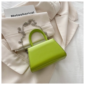 Detail of a bright green mini trapeze handbag with silver chain strap and top handle