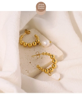 Macro shot of gold-plated beaded C-shape earrings featuring white baroque pearl accents