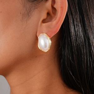 Gros plan d'un mannequin portant de grandes boucles d'oreilles perles ovales bordées d'or