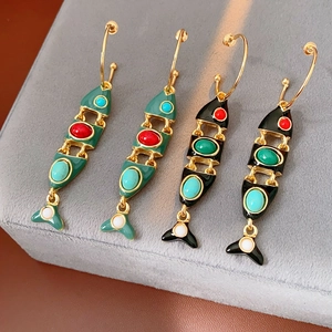 Detail of vintage enamel fish bone earrings with colorful gemstones on a velvet stand