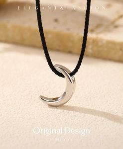 Close-up of crescent moon necklace with black woven cord on cream textured stone