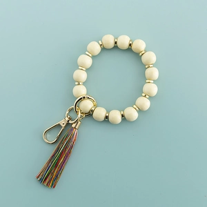 Détail de porte-clés en perles de bois crème avec pompon coloré et boucle dorée