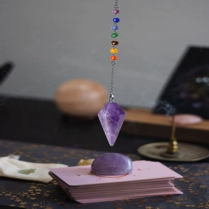 Amethyst pendulum with chakra stones hanging over tarot cards in a mystical setting