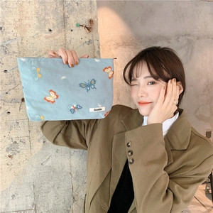 Detail of light blue embroidered butterfly makeup bag with zipper held by a model