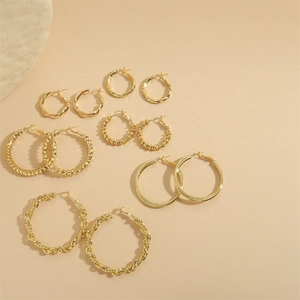 Set of 6 gold hoop earrings in various twisted and beaded designs on beige background
