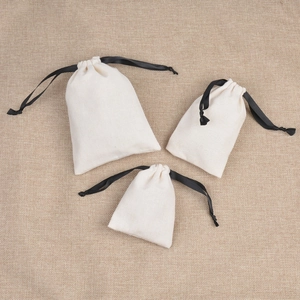 Three cream cotton drawstring jewelry bags in different sizes on rustic linen background
