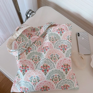 Flat lay of floral canvas tote bag with bohemian mandala prints and accessory on a desk