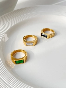 Detail of three stainless steel rings with emerald, zircon and black stone in a white ceramic dish