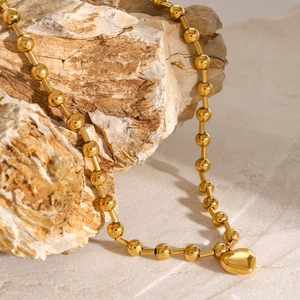 Macro shot of gold beaded heart necklace displayed on textured natural beige stone