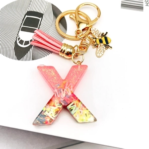 Detailed close-up of pink resin letter X keychain with glitter, tassel, and bee charm