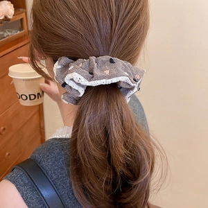 Detailed view of grey fabric scrunchie with lace trim on a model high ponytail