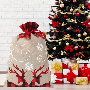 Large jute Christmas gift bag with red black plaid deer and snowflakes by a tree