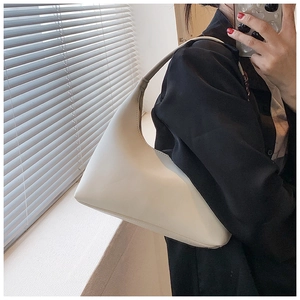 Close-up of a minimalist cream-colored crescent underarm bag worn on the shoulder