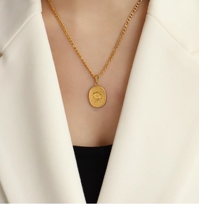 Gros plan d'un pendentif rose ovale doré sur une chaîne Figaro porté sur un blazer blanc