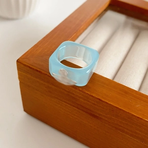 Close-up of a light blue square resin ring with silver saturn logo on a wooden display