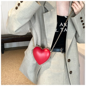 Close-up of red heart-shaped leather crossbody bag with gold chain strap on a model