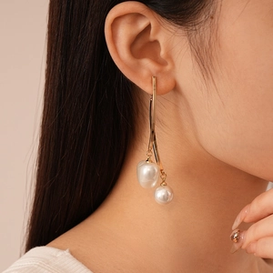 Close-up of gold dangle earrings with two white pearls on a model in high detail