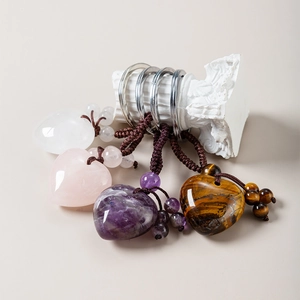 Detail of four natural crystal heart keychains in rose quartz, amethyst, and tiger eye stone