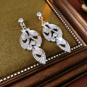 Macro shot of silver leaf-shaped earrings with crystals on a green fabric stand