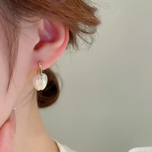 Gros plan d'élégantes boucles d'oreilles cœur en perles dorées portées par un mannequin