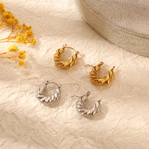 Chic twisted hoop earrings in gold and silver finish on soft textured fabric background