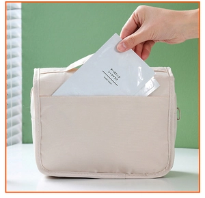 Detail showing hand placing sheet mask into front pocket of beige travel toiletry bag