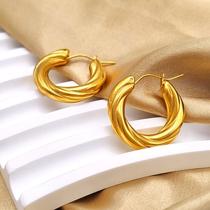 Detail of gold twisted hoop earrings showing mirror-polished texture on silk fabric