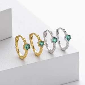 Detailed view of silver and gold earrings with green gemstones on minimalist display