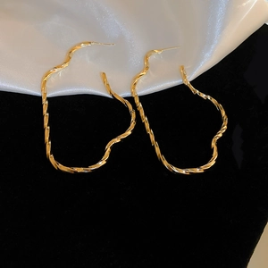 Detail shot of large golden irregular wave-textured hoop earrings on silk background