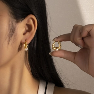 Detailed view of vintage gold wavy earrings with white pearls on a female model