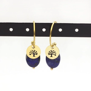 Macro shot of gold Tree of Life charm earrings with blue lapis lazuli stones on a stand