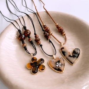 Detailed view of amber resin flower and heart pendants on leather cords in a ceramic tray
