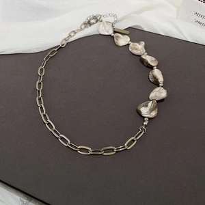 Dettaglio della collana con catena argentata e perle in conchiglia su fondo grigio