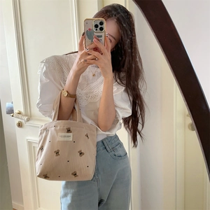 Beige corduroy handbag with bear embroidery held by a model in a casual lifestyle setting