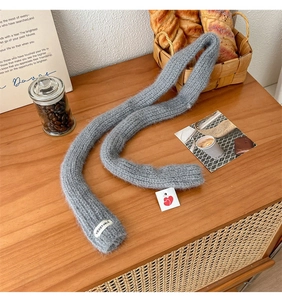 Detail of grey knitted scarf with soft texture and beige vegetable label on wooden desk