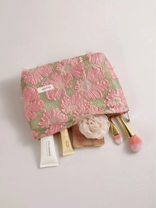 Pink floral embroidery makeup bag with green background and makeup brushes around