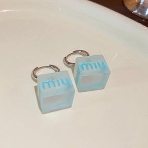 Detailed macro view of light blue heart cube earrings with silver clasps on white table