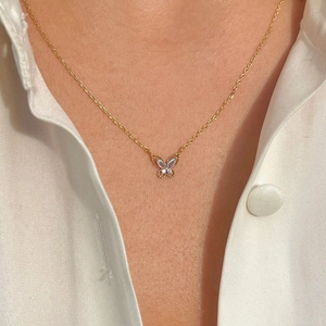 Close-up of gold-plated butterfly pendant necklace featuring an iridescent inlay on a model
