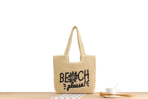 Détail du sac cabas en paille tressée avec broderie noire BEACH please! sur bois
